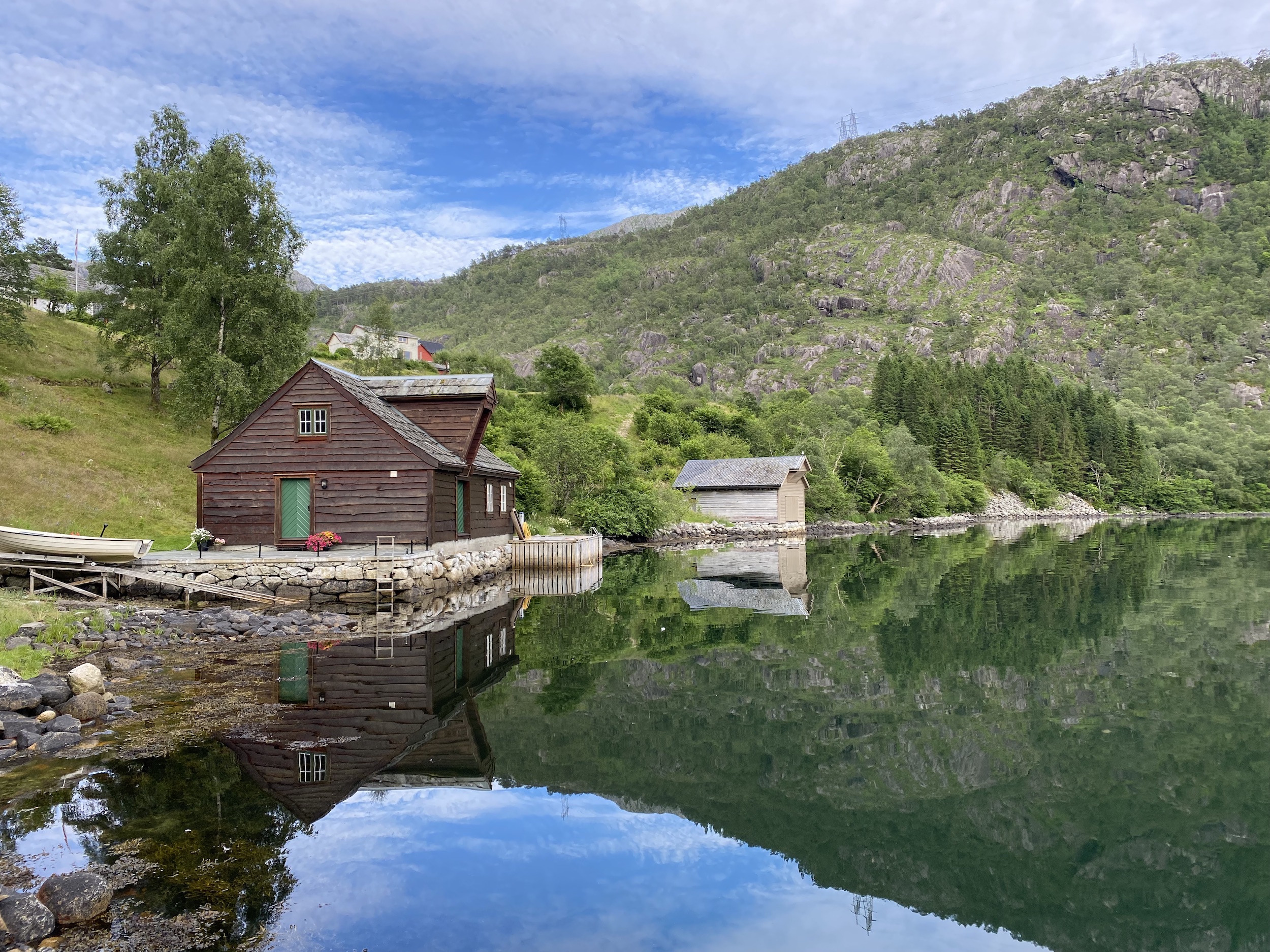 To naust som ligger ved vannkanten, med fjell i bakgrunn